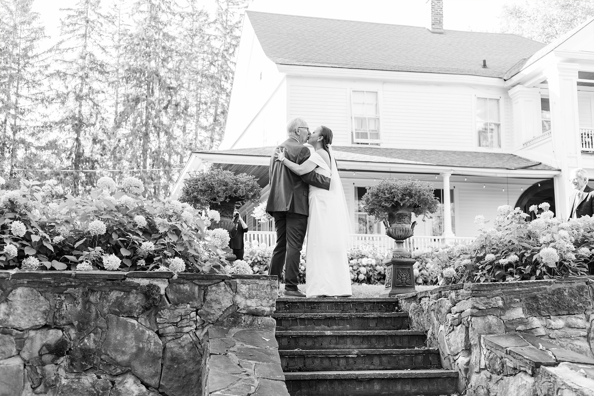 bride and groom sharing kiss in front of venue manor at the top of stone stairs