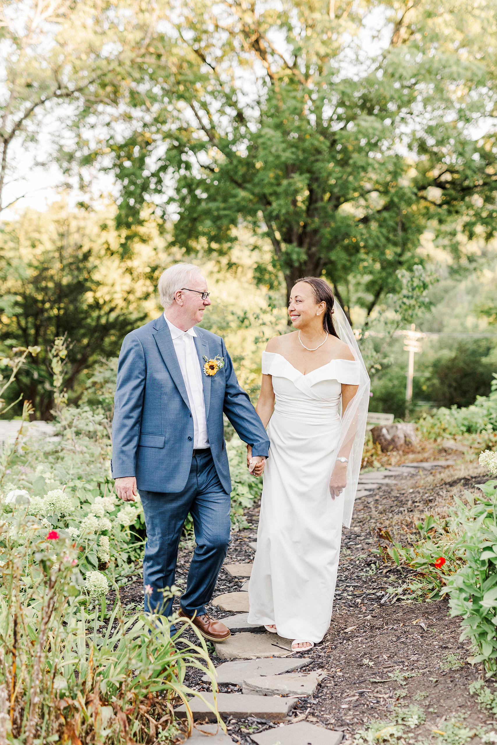 bride and from walking hand in hand on stone path surrounded by greenery
