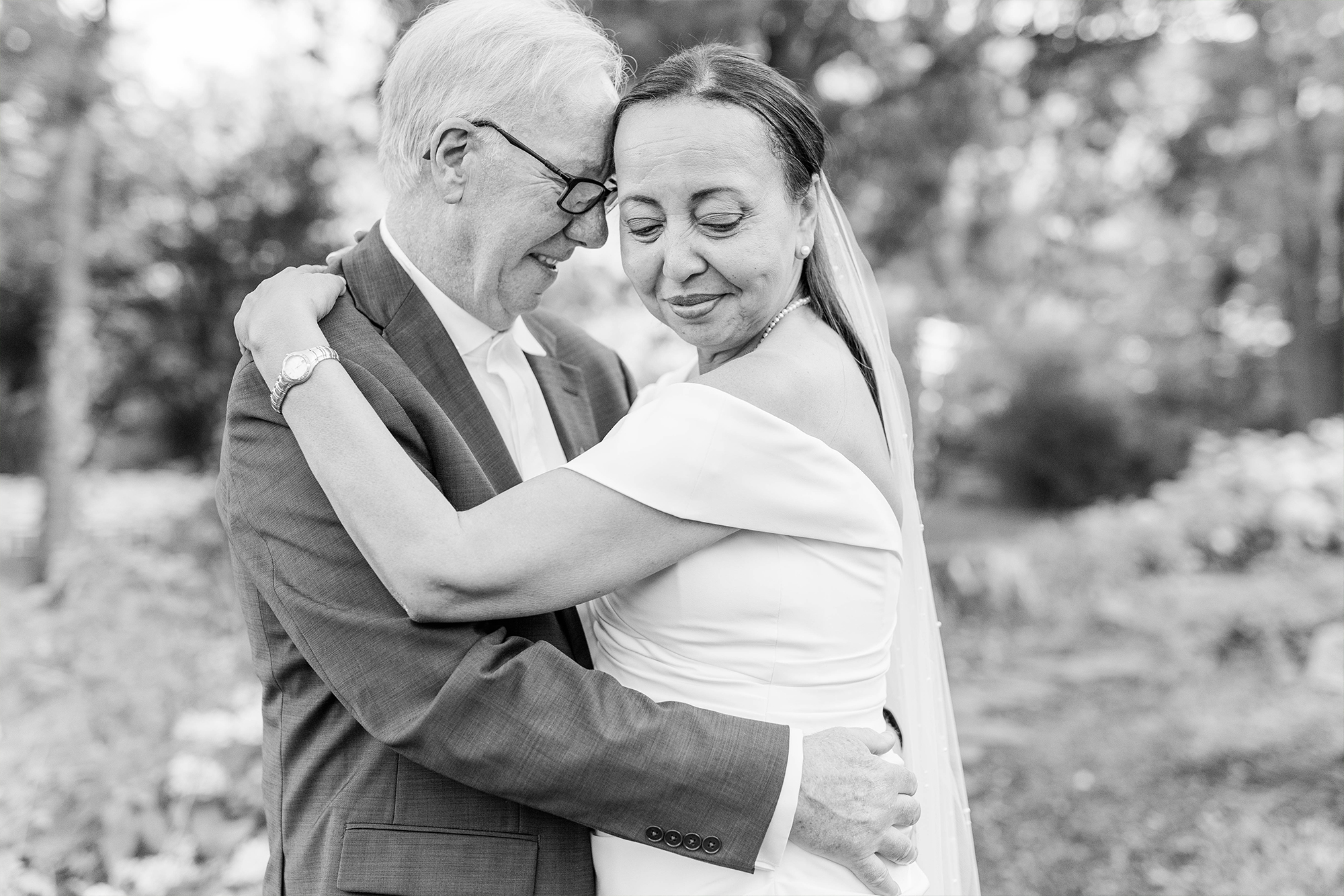bride and groom foreheads resting against another surrounded by greenery