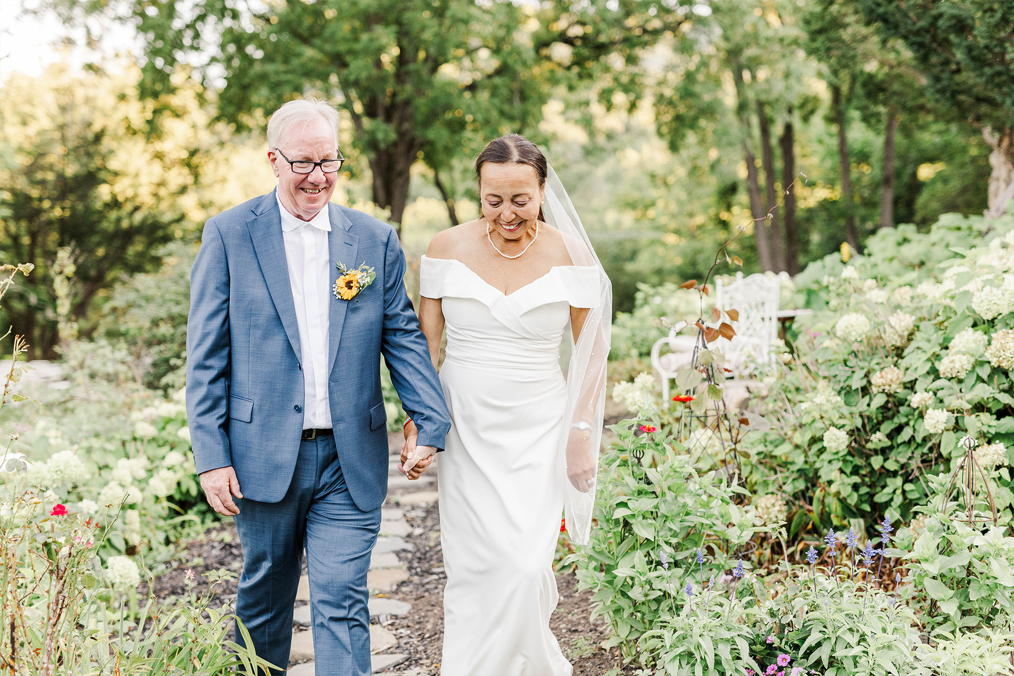 bride and groom walking hand in hand on stone path with bushes and trees