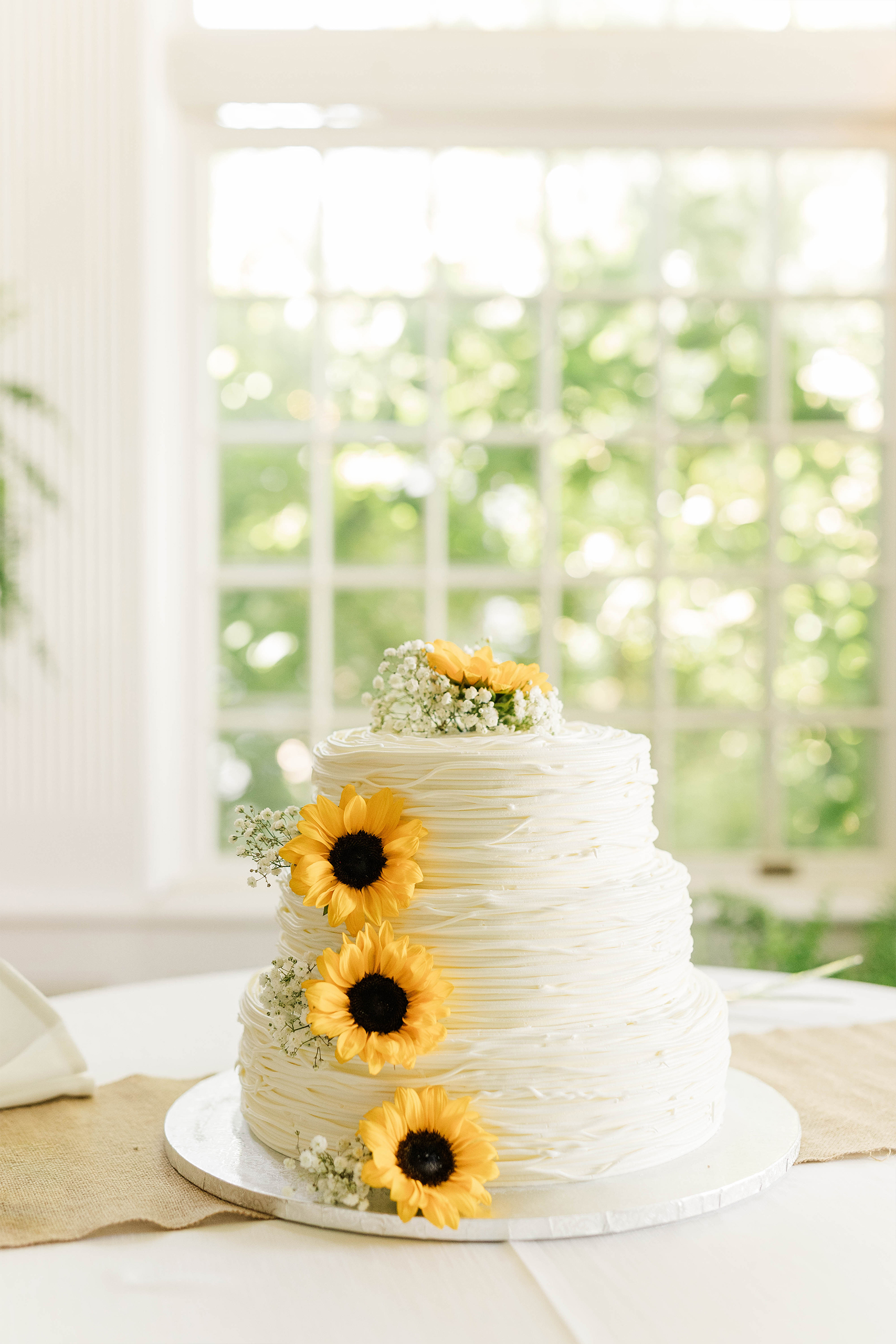 three layered wedding cake with floral details in white space with window with greenery