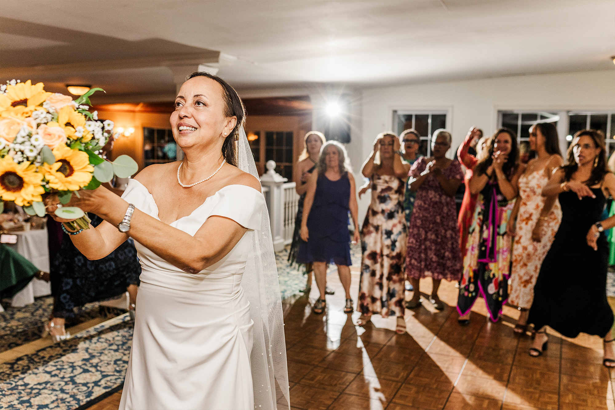 bride with bouquet at bouquet toss with wedding guests behind her