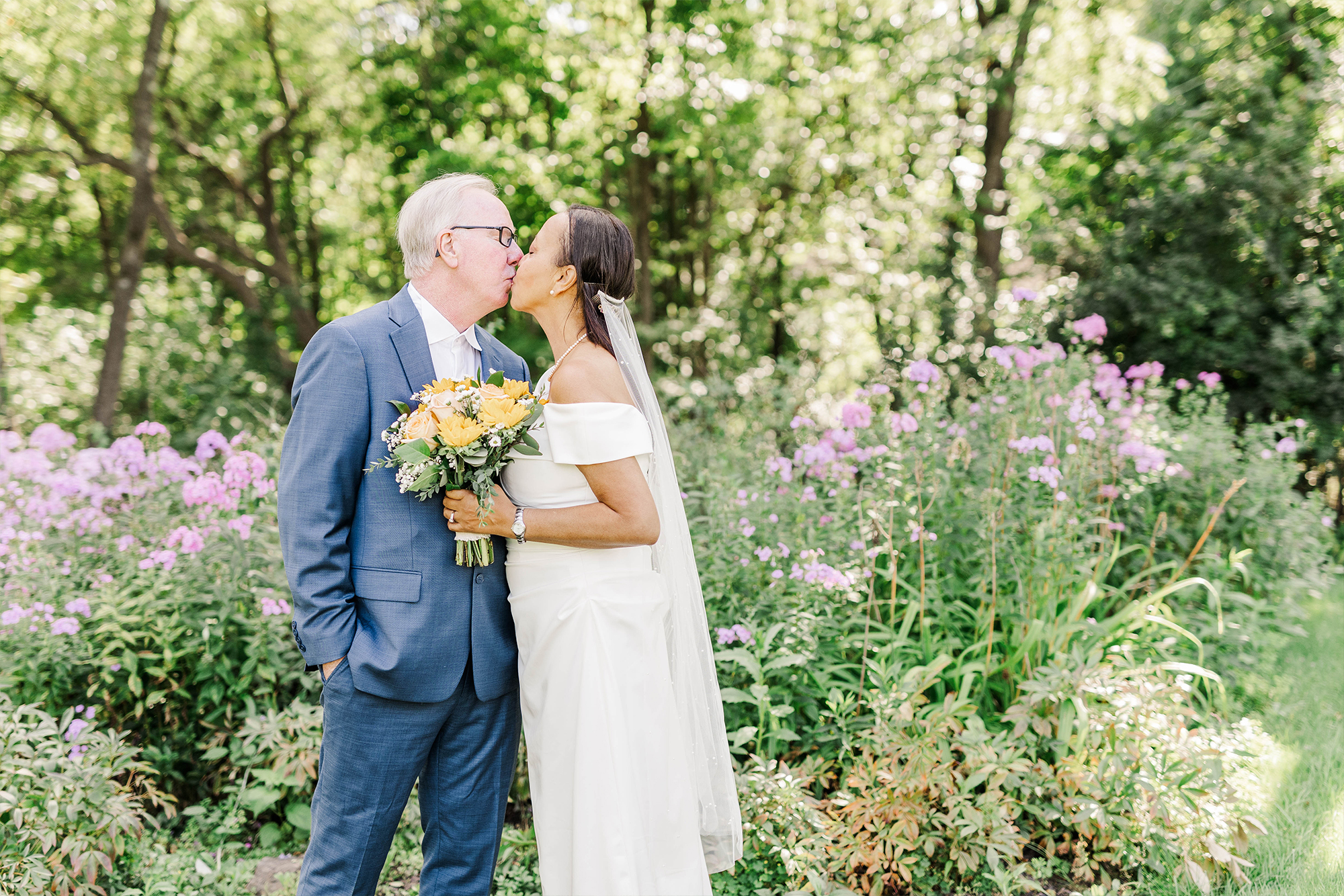 bride and groom sharing kiss in front of tall greenery
